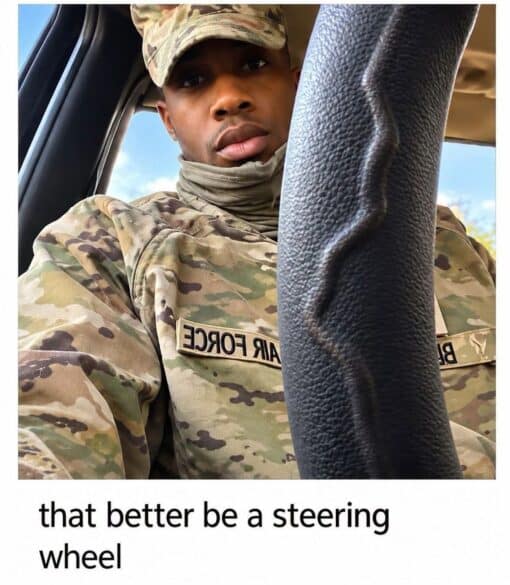 Auto Parts Memes, Car Memes, Dirty Mind Memes, Double Meaning Memes, Driving Memes, Funniest Memes, Innuendo Memes, Military Memes, Misunderstanding Memes, Soldier Memes, WTF Memes, A uniformed Air Force service member sits in what appears to be a vehicle, looking directly at the camera with a serious, slightly puzzled expression. A large black steering wheel or column dominates the foreground, cutting vertically through the right side of the image and partly blocking the view of his uniform.