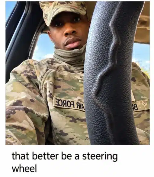 Auto Parts Memes, Car Memes, Dirty Mind Memes, Double Meaning Memes, Driving Memes, Funniest Memes, Innuendo Memes, Military Memes, Misunderstanding Memes, Soldier Memes, WTF Memes, A uniformed Air Force service member sits in what appears to be a vehicle, looking directly at the camera with a serious, slightly puzzled expression. A large black steering wheel or column dominates the foreground, cutting vertically through the right side of the image and partly blocking the view of his uniform.
