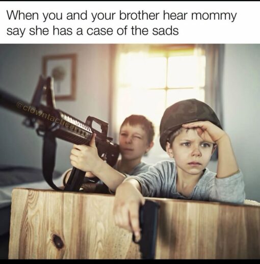Brother Memes, Dark Humor, Depression Memes, Family Memes, Funniest Memes, Gun Memes, Kid Memes, Kids vs Parents Memes, Mom Memes, Parent Memes, Sad, Sibling Memes, The meme shows two young boys crouched behind a wooden crate in a softly lit room, staged like tiny soldiers in a dramatic action scene. One boy in the background aims a large rifle forward, while the boy in front wears a helmet, looks intensely serious, and appears to hold a pistol over the edge of the crate.
