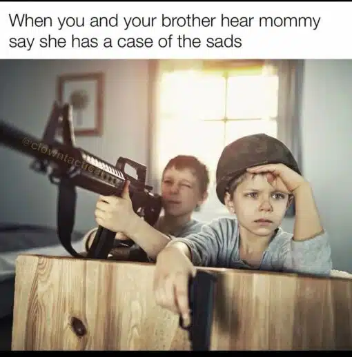 Brother Memes, Dark Humor, Depression Memes, Family Memes, Funniest Memes, Gun Memes, Kid Memes, Kids vs Parents Memes, Mom Memes, Parent Memes, Sad, Sibling Memes, The meme shows two young boys crouched behind a wooden crate in a softly lit room, staged like tiny soldiers in a dramatic action scene. One boy in the background aims a large rifle forward, while the boy in front wears a helmet, looks intensely serious, and appears to hold a pistol over the edge of the crate.