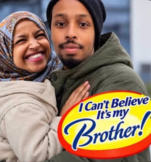 Brother Memes, Commercial Memes, Family Memes, Food Memes, Funniest Memes, Ilhan Married Her Brother, Incest Memes, Play on Words Memes, Political Memes, Pun Memes, Sibling Memes, The meme shows a close-up photo of a woman in a patterned headscarf grinning broadly while holding onto a man in a dark beanie and green winter jacket. The two are posed very close together, giving the image an affectionate, couple-like feel at first glance. In the lower-right corner, a bright yellow oval label with a red border and blue lettering has been edited over the photo like a product logo. The text reads, “I Can't Believe / It's my / Brother!” with “Brother!” enlarged in a sweeping script for extra emphasis.