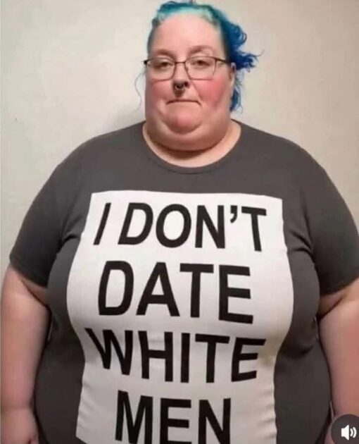 Dating Memes, Fat Joke Memes, Funniest Memes, Men vs Women, Offensive Memes, Racist Memes, Relationship Memes, Stereotype Memes, White People Memes, Women Memes, A person with bright blue hair, glasses, and a septum piercing stands facing the camera against a plain, light-colored wall. They wear a dark T-shirt with a large white rectangular panel across the front, printed in oversized black capital letters: “I DON’T DATE WHITE MEN.” The image has a blunt, confrontational feel because the text dominates the frame and reads like a personal rule or slogan. The person’s neutral expression and straightforward pose make the shirt’s message feel even more deadpan and intentionally provocative.