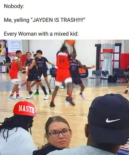 Angry Memes, Funniest Memes, Insult Memes, Kid Memes, Mom Memes, Nasty Memes, Offensive Memes, Roast Memes, Sports Memes, Stereotype Memes, Women Memes, The meme uses a classic “Nobody:” setup in large black text over a blurry youth basketball game. On the court, kids are mid-play, while the foreground focuses on spectators sitting courtside, especially a woman in glasses turning around with a sharp, stunned glare. A red hat graphic labeled “NASTIE” is placed over someone in the crowd, adding a loud reaction-caption feel to the scene. The whole image looks like a screenshot from a chaotic gym moment where one shouted insult instantly pulls attention from the audience.