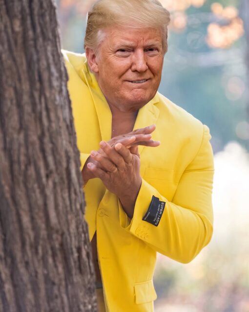 AI Memes, Donald Trump Memes, Fashion Memes, Funniest Memes, Funny Text Memes, Internet Memes, Mashup Memes, Political Memes, Style Memes, Trump and Nicki’s Ass, Weird Memes, WTF Memes, The image shows Donald Trump’s face composited onto the familiar “man in a yellow suit hiding behind a tree” meme pose. He is peeking from behind a large tree trunk, rubbing his hands together with a pleased, scheming expression, while wearing an extremely bright yellow suit jacket against a soft, blurred outdoor background. A small black clothing tag is still attached to the jacket sleeve, making the suit look fresh off the rack. The tag reads: “SUPER.IAST15 / CLASSIC SUITING / WASHABLE / PERMANENT PRESS,” adding a weird retail-label detail to an already exaggerated, staged-looking image.